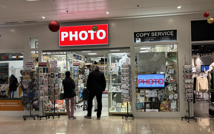 La fachada de Photo Planète Charmilles en la galería del centro comercial, rótulo rojo PHOTO y panel Copy Service